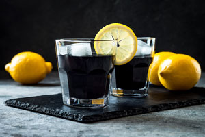 Due bicchieri di limonata carbone attivo su una fetta nera con 2 limoni accanto