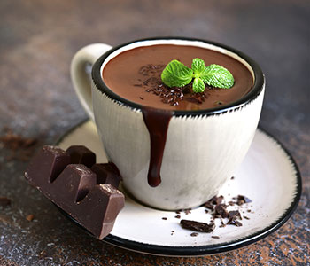 cioccolata fondente calda in tazza bianca con foglia di menta sopra e ttavoletta di cioccolata accanto