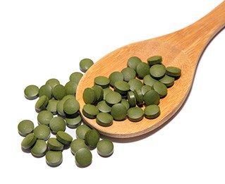 capsule verdi di clorella su un cucchiaio marrone di legno