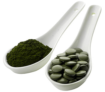 Due cucchiai di porcellana bianca, uno riempito con polvere di clorella verde e l'altro con pillole verdi Due cucchiai di porcellana bianca, uno riempito con polvere di clorella verde e l'altro con pillole verdi