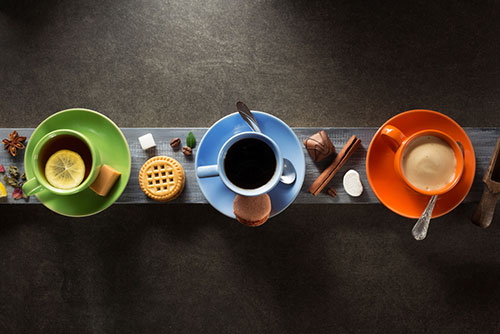 Tazza verde con il tè blu della tazza con il caffè arancio della tazza con latte e i biscotti intorno