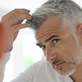 uomo con capelli brizzolati che si tocca la testa e i capelli