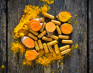 polvere arancione in ciotole e capsule di curcuma su tavolo marrone