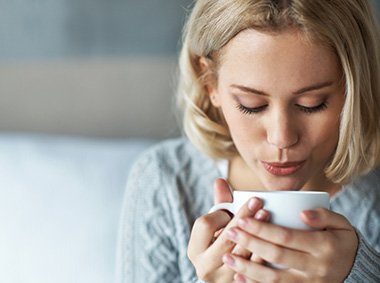 donna che beve infuso caldo seduta sul letto in pigiama