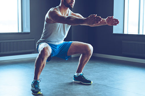 uomo in palestra facendo squat con le braccia tese