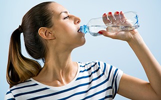 donna in pigiama che beve acqua da bottiglietta di plastica