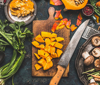 zucca tagliata a pezzi sul tagliere con foglie e altri ingredienti intorno