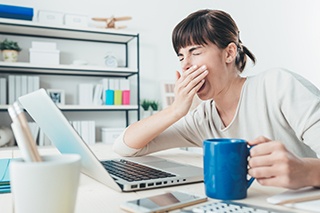 donna seduta al computer che sbadiglia mentre è davanti al pc