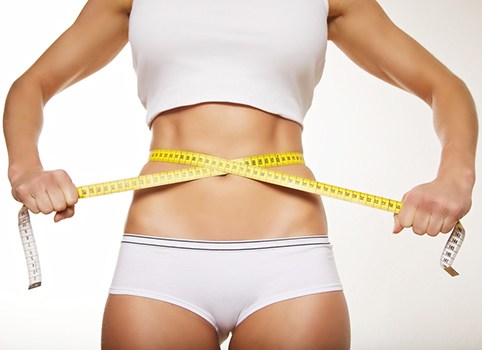 corpo di donna in abiti da palestra bianchi che si misura la circonferenza con un metro