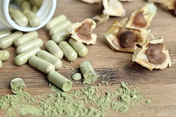 capsule verdi di moringa con polvere verde che esce su un tavolo marrone