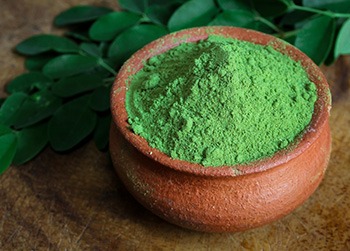 polvere verde di moringa in una ciotola e foglie di moringa spezzettate