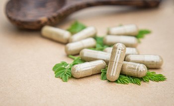 capsule verdi di moringa con polvere verde che esce su un tavolo marrone